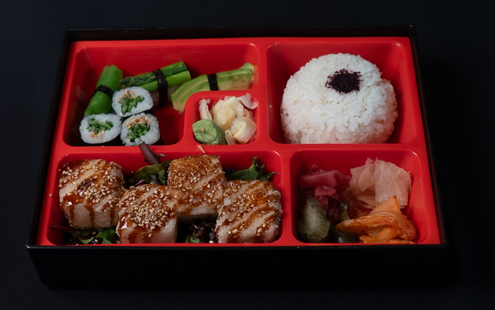 Hurley House - A bento box with sushi rolls, steamed vegetables, white rice topped with a dark garnish, grilled tofu with sesame seeds, and assorted pickled vegetables, all arranged in separate red compartments.