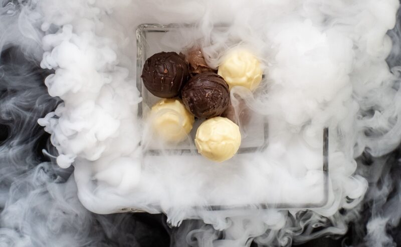 Hurley House - A hand pours liquid from a white pitcher over a glass dish holding chocolate and white truffles, surrounded by dramatic swirling vapor, likely caused by dry ice.