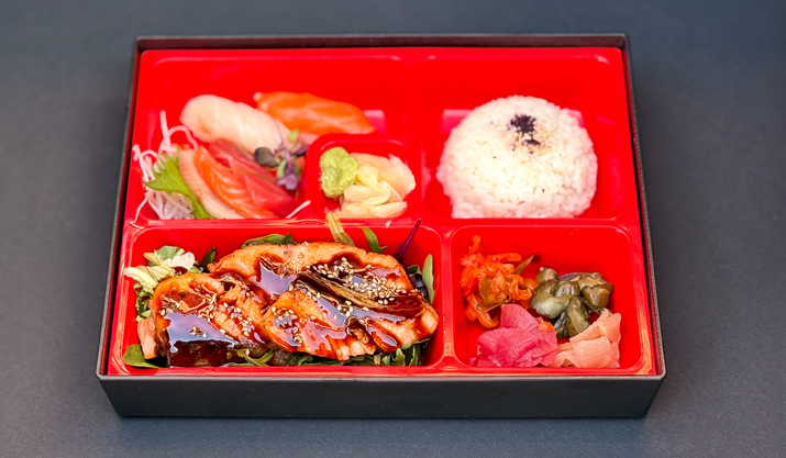 Hurley House - A red bento box with compartments holding white rice, sushi, glazed grilled eel, pickled vegetables, ginger, wasabi, and a garnish, set against a dark background.